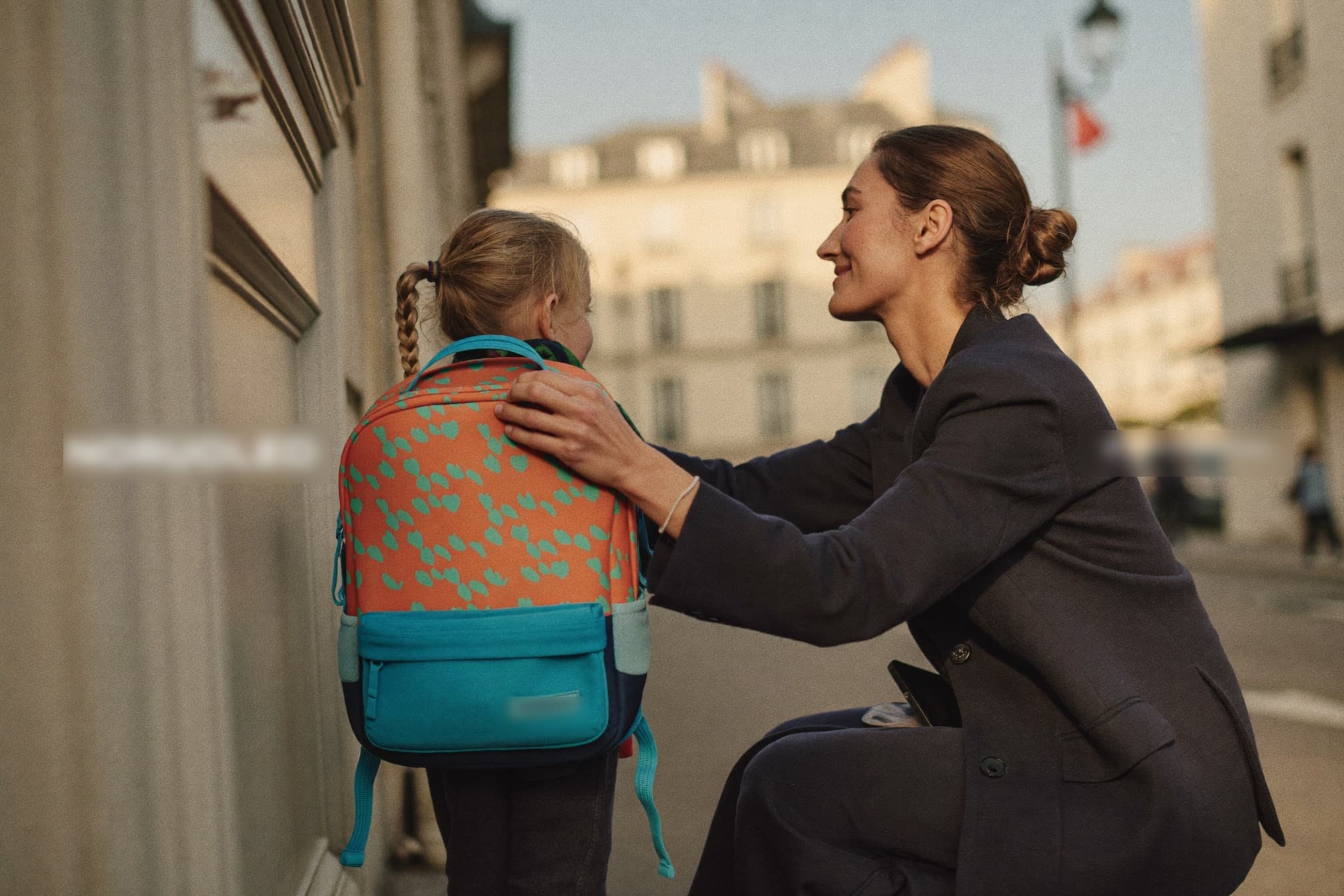 Une maman ajuste le cartable de sa fille avant le départ pour l'école, dans la lumière du matin.